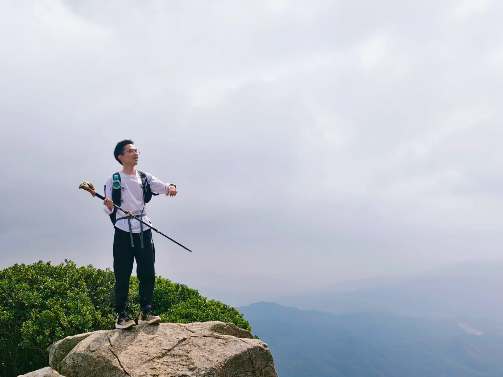羅卓手持登山杖站在山顶岩石上